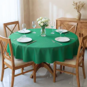 Mesa de madeira de 4 lugares arrumada com toalha de mesa redonda verde. Cenário clean com louças, taças e vaso de rosas.