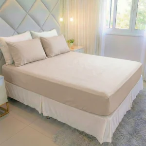 Cama king com jogo de lençol king 400 fios nude Cozzilar em quarto moderno com cabeceira cinza estofada, saia-cama branca e tapete felpudo.