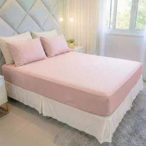 Cama king com jogo de lençol king 400 fios rosê Cozzilar em quarto moderno com cabeceira cinza estofada, saia-cama branca e tapete felpudo.